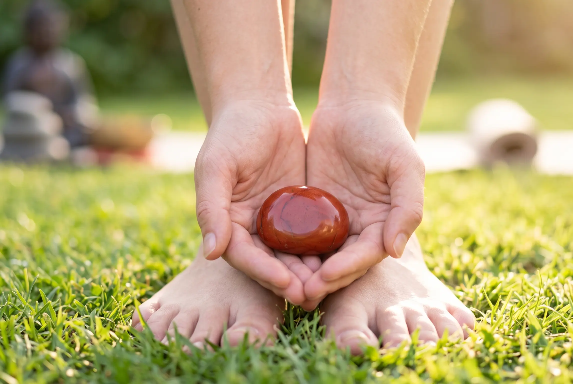 Red Jasper stone held against barefoot standing on grass for grounding and stamina.