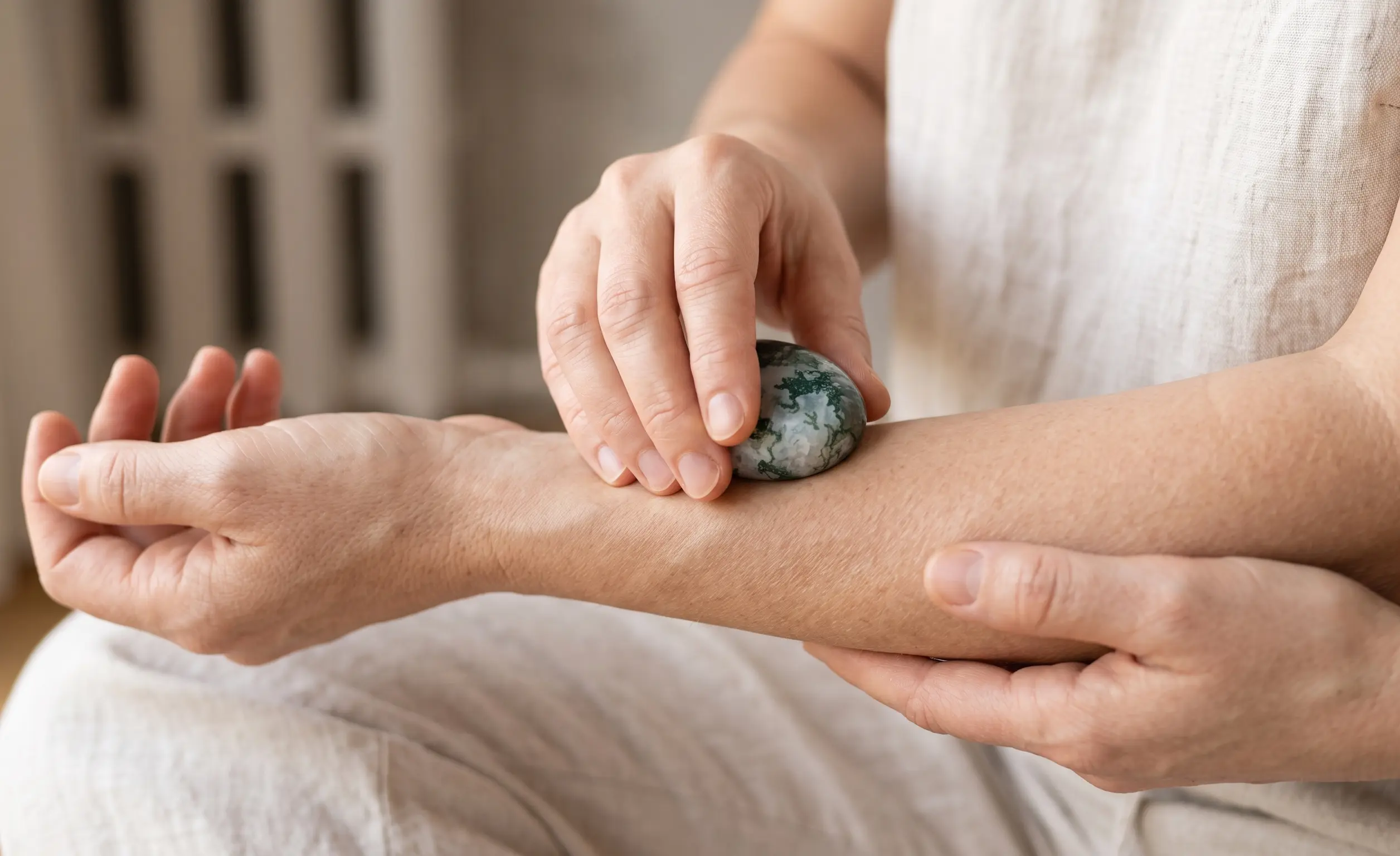 A cinematic close-up of relaxed hands gently pressing a smooth Moss Agate stone against a softened muscle knot in the forearm, visualizing relief and circulation flow.